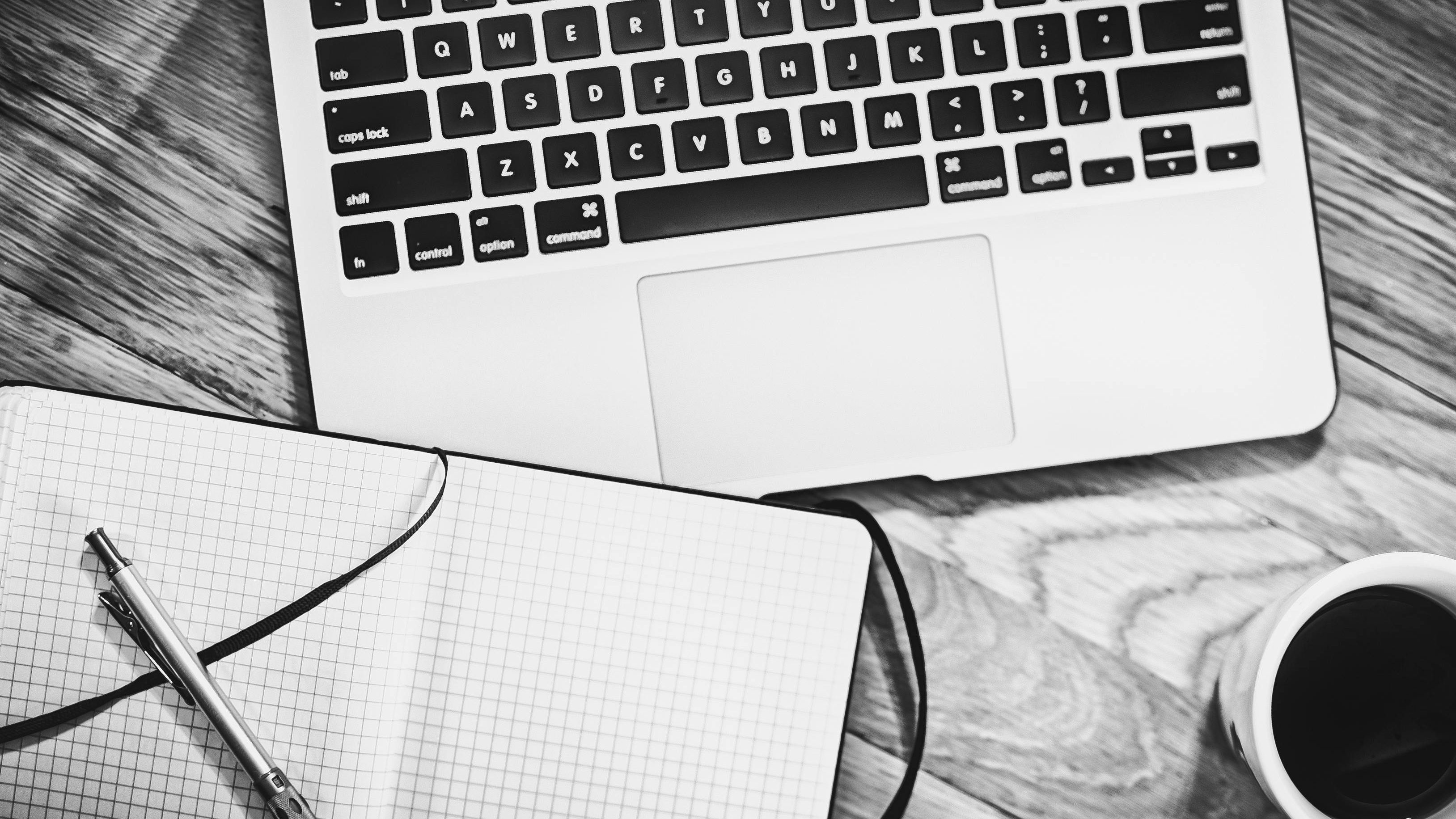 Laptop und Notizbuch auf einem Schreibtisch, gemeinsam mit einer Tasse Kaffee